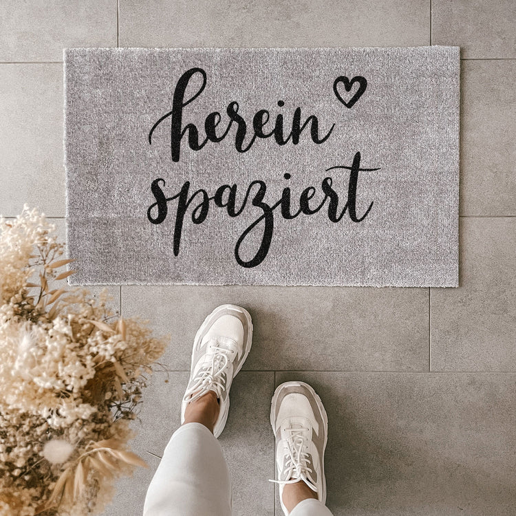 Gray washable doormat with "hereinspaziert" slogan in black script, unique style and cozy home decor. - Waschbare Fußmatte Hereinspaziert