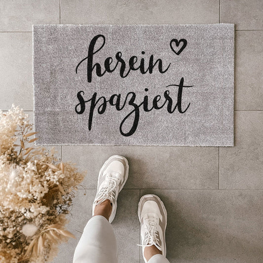 Gray washable doormat with "hereinspaziert" slogan in black script, unique style and cozy home decor. - Waschbare Fußmatte Hereinspaziert