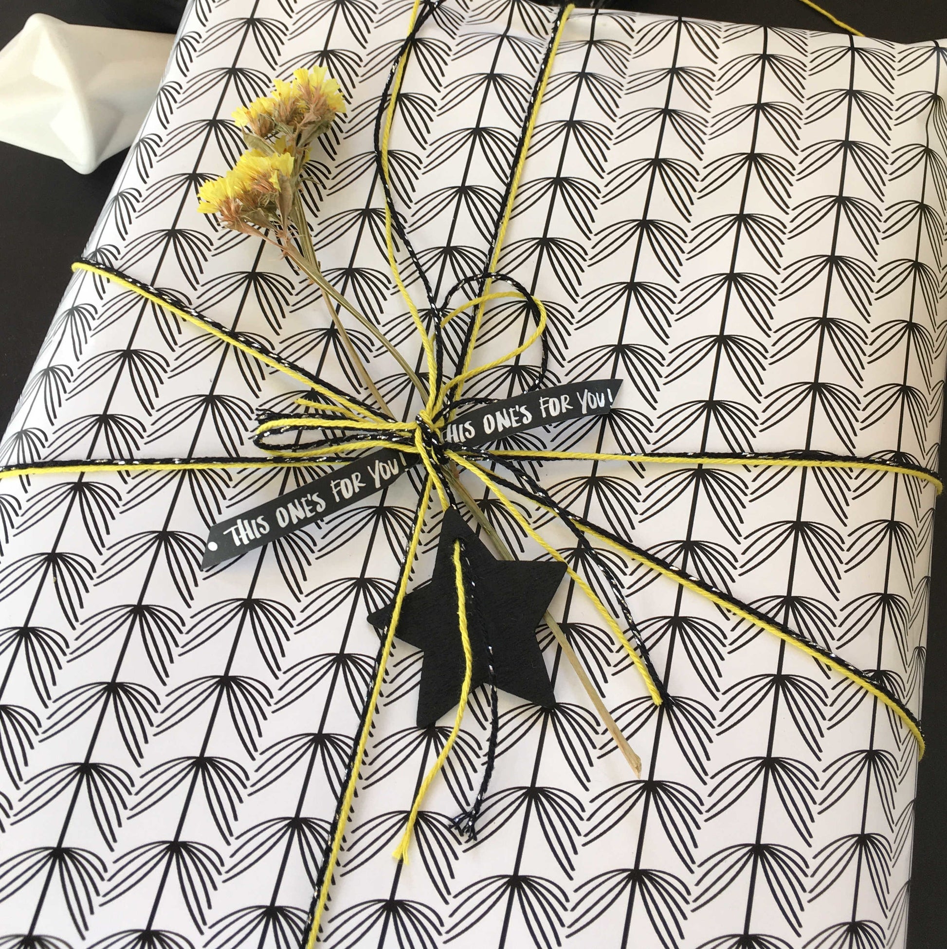 Gift wrapped in black and white patterned paper with yellow string, showcasing einzigartig Wohndeko for individueller Stil. - Geschenkverpackung